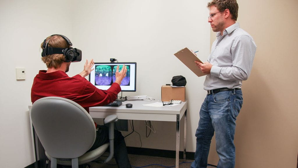 person with clipboard observing another person on a VR computer experience