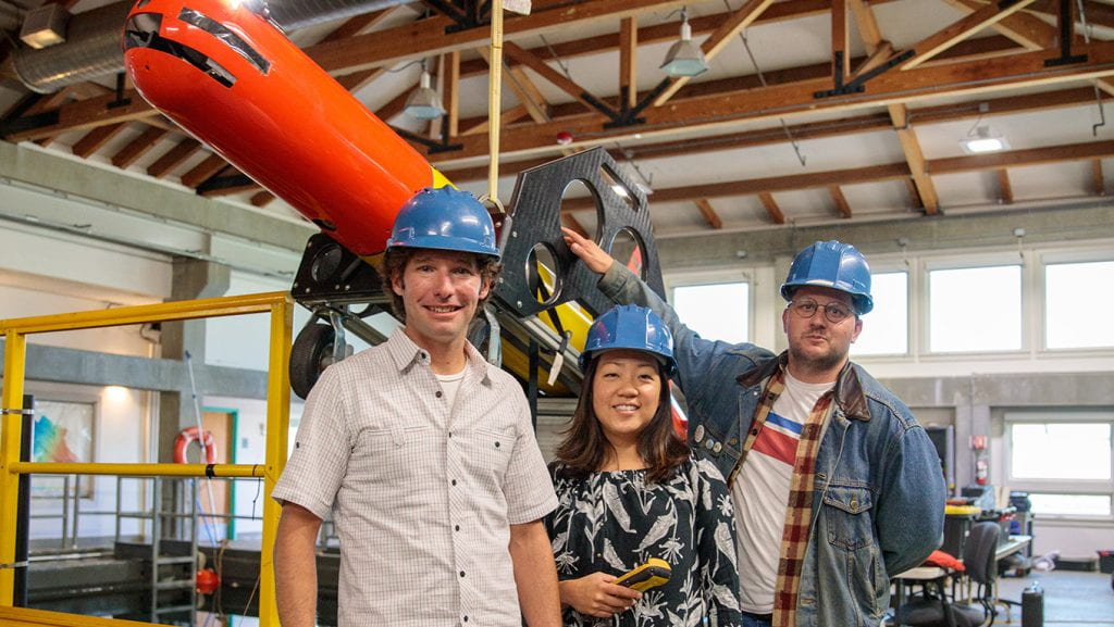 three people with hardhats in front of machinery 